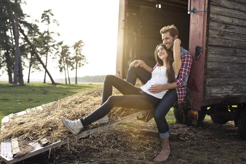 Glückliches junges Paar auf einem Wohnwagen auf dem Lande sitzend - PNEF01332