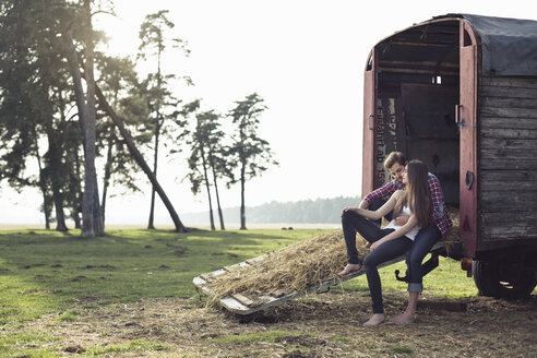 Glückliches junges Paar auf einem Wohnwagen auf dem Lande sitzend - PNEF01333