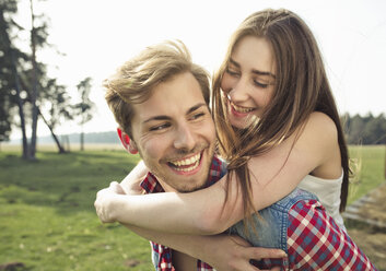 Happy young man carrying girlfriend piggyback on meadow - PNEF01336