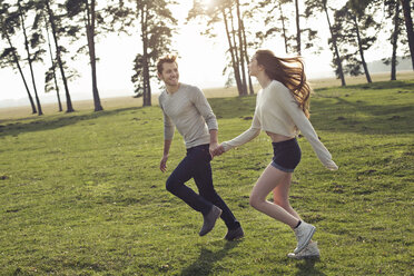 Happy young couple running hand in hand on meadow - PNEF01338