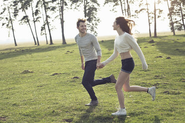 Happy young couple running hand in hand on meadow - PNEF01339