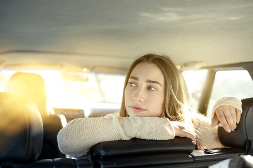 Junge Frau sitzt auf dem Rücksitz im Auto und schaut zur Seite - PNEF01340