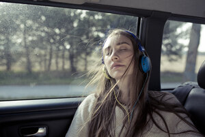 Young woman with windswept hair in a car wearing headphones - PNEF01342