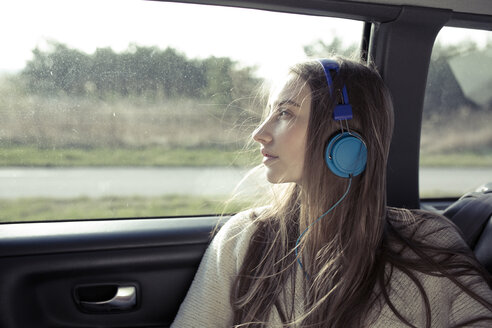 Junge Frau mit zerzaustem Haar in einem Auto und Kopfhörern - PNEF01343