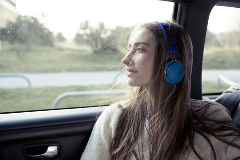 Junge Frau mit zerzaustem Haar in einem Auto und Kopfhörern - PNEF01344