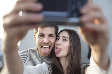 Verspieltes junges Paar macht ein Selfie und streckt die Zungen heraus - PNEF01346