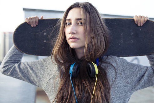 Porträt einer ernsten jungen Frau mit Skateboard und Kopfhörern - PNEF01353