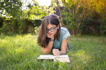 Girl lying on a meadow in garden reading book - LVF07894