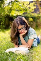 Mädchen liegt auf einer Wiese im Garten und liest ein Buch - LVF07895