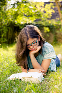 Girl lying on a meadow in garden reading book - LVF07895