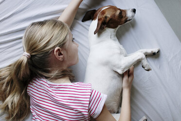 Blondes Mädchen auf dem Bett liegend kitzelt ihren Hund - JPF00374