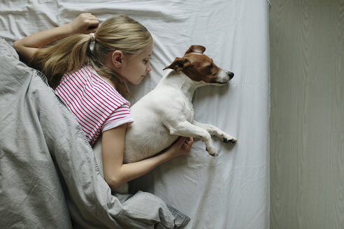 Blond girl lying on bed with her dog sleeping, top view - JPF00378