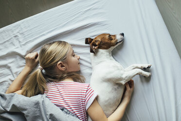 Blond girl lying on bed with her dog sleeping, top view - JPF00379