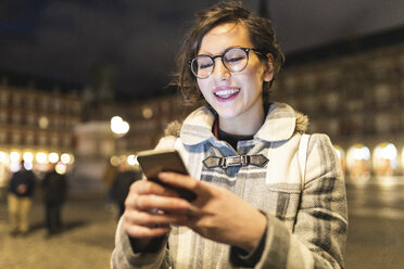 Spanien, Madrid, Plaza Mayor, glückliche junge Frau, die ihr Smartphone benutzt - WPEF01388