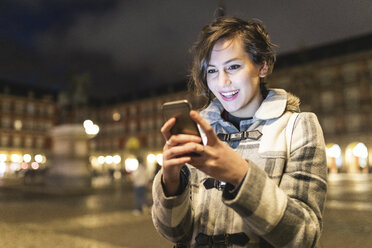 Spanien, Madrid, Plaza Mayor, glückliche junge Frau, die ihr Smartphone benutzt - WPEF01389
