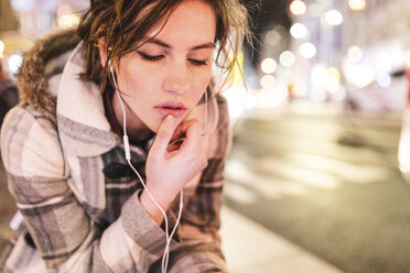 Spain, Madrid, young woman in the city at night wearing earphones - WPEF01396