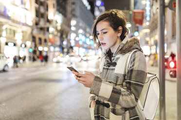 Spanien, Madrid, junge Frau in der Stadt, die nachts ihr Smartphone benutzt - WPEF01400
