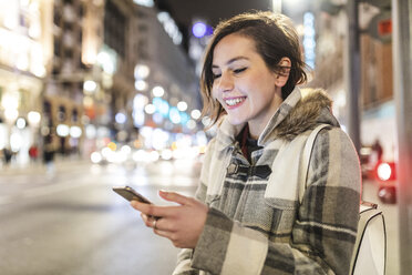 Spain, Madrid, young woman in the city at night using her smartphone - WPEF01401
