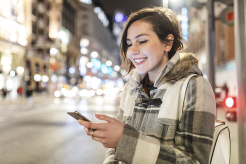 Spanien, Madrid, junge Frau in der Stadt, die nachts ihr Smartphone benutzt - WPEF01401