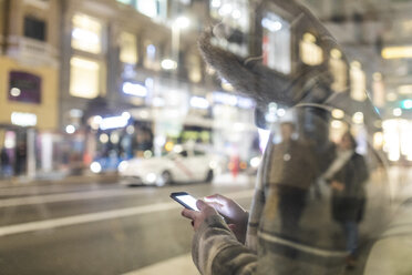 Spanien, Madrid, junge Frau in der Stadt bei Nacht neben der Gran Via, die ihr Smartphone benutzt - WPEF01404