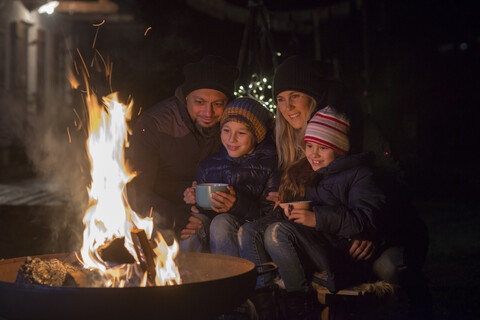 Familie mit Tassen, die abends am Feuer sitzen, lizenzfreies Stockfoto