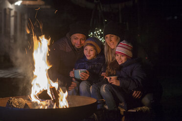 Familie mit Tassen, die abends am Feuer sitzen - LBF02499