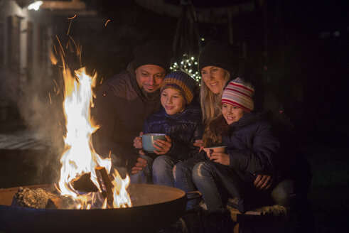 Family with mugs sitting at the fire at night - LBF02499