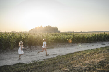 Girl and boy running on a rural dirt track along cornfield - EYAF00053