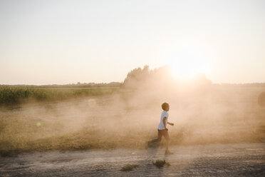 Junge läuft auf einem Feldweg bei Sonnenuntergang - EYAF00054