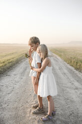 Mädchen umarmt Jungen auf einem ländlichen Feldweg - EYAF00058