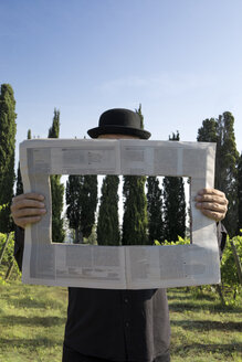 Italien, Toskana, unsichtbarer Mann umgeben von Zypressen, der eine Zeitung mit einem Loch liest - PSTF00329