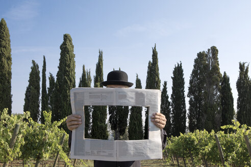 Italien, Toskana, unsichtbarer Mann umgeben von Zypressen, der eine Zeitung mit einem Loch liest - PSTF00330