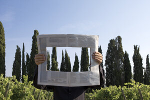 Italy, Tuscany, invisible man surrounded by cypresses reading newspaper with a hole - PSTF00331