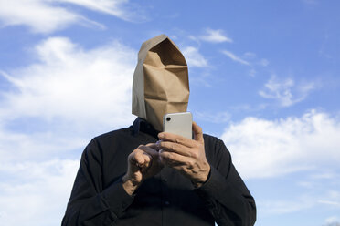 Mann mit Papiertüte über dem Kopf, der ein Mobiltelefon benutzt - PSTF00362