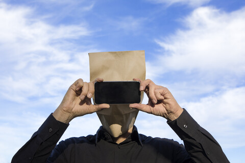 Mann mit Papiertüte über dem Kopf, der ein Mobiltelefon benutzt, lizenzfreies Stockfoto