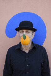 Portrait of man with an orange at a wall with question mark wearing a bowler hat - PSTF00368