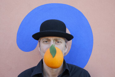 Portrait of man with an orange at a wall with question mark wearing a bowler hat - PSTF00369