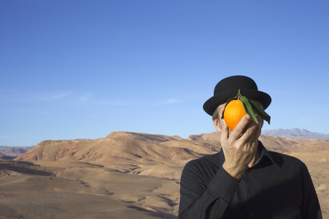 Morocco, Ounila Valley, man wearing a bowler hat holding an orange in front of his face stock photo