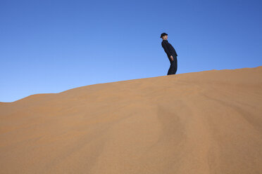 Morocco, Merzouga, Erg Chebbi, man wearing a bowler hat standing crooked on desert dune - PSTF00392