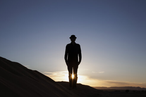 Morocco, Merzouga, Erg Chebbi, silhouette of man wearing a bowler hat standing on desert dune at sunset - PSTF00404