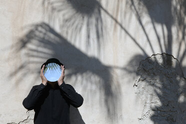 Marokko, Essaouira, Mann mit Melone, der sich an einer Wand einen Spiegel vor das Gesicht hält - PSTF00412
