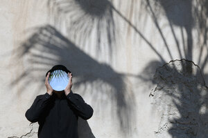 Morocco, Essaouira, man wearing a bowler hat holding mirror in front of his face at a wall - PSTF00412