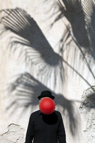 Morocco, Essaouira, man wearing a bowler hat with red balloon in front of his face at a wall stock photo