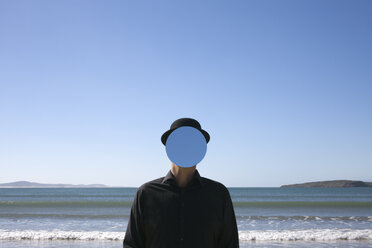 Morocco, Essaouira, man wearing a bowler hat with mirror in front of his face at the sea - PSTF00424