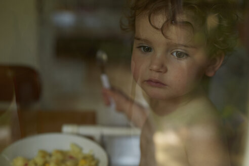 Tagträumendes kleines Mädchen hinter einer Fensterscheibe beim Mittagessen - AMEF00039
