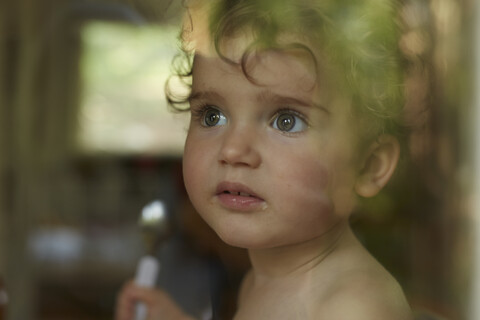 Portrait of little girl behind windowpane eating stock photo