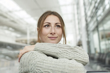 Porträt einer lächelnden jungen Frau auf dem Flughafen, die im Wartebereich sitzt - PNEF01365