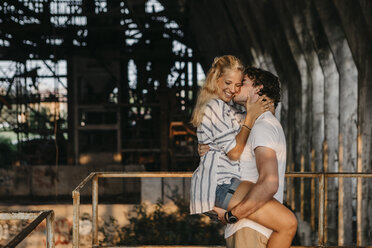 Young man carrying and kissing girlfriend in an old train station - LHPF00518