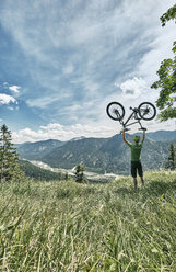 Deutschland, Bayern, Isartal, Karwendelgebirge, Mountainbiker bei einem Ausflug, der sein Fahrrad auf einer Almwiese hochhebt - WFF00071