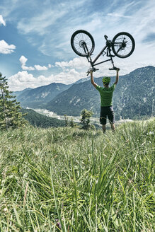 Deutschland, Bayern, Isartal, Karwendelgebirge, Mountainbiker bei einem Ausflug, der sein Fahrrad auf einer Almwiese hochhebt - WFF00075